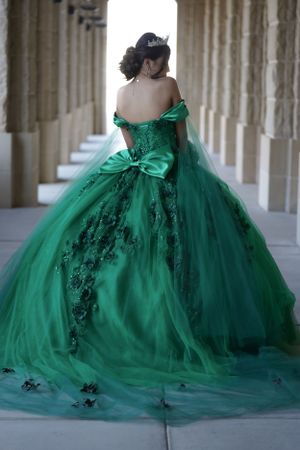 Emerald green ball gown with intricate details photographed in a columned hallway.