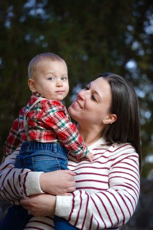 Tender moment between parent and child wearing red plaid shirt and overalls in outdoor setting.