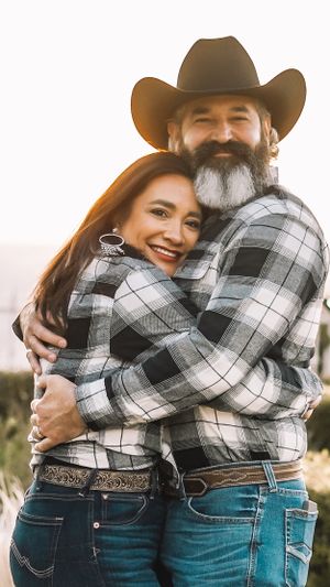Couple in matching plaid shirts and denim share intimate embrace outdoors.
