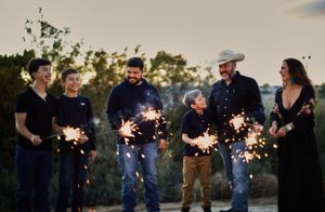 Group silhouettes holding sparklers against sunset sky creating festive light trails.