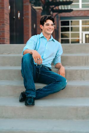Person in light blue shirt and jeans relaxing on concrete steps outdoors.
