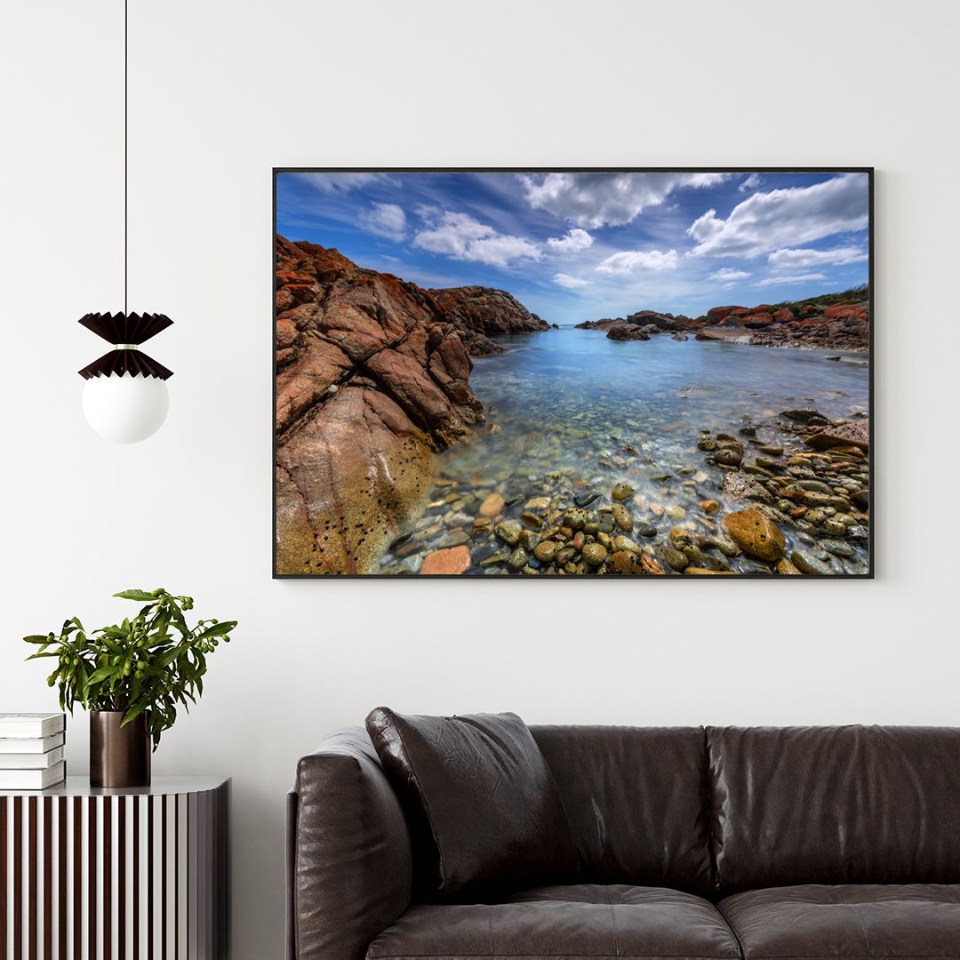 Crystal clear tide pool surrounded by red rocky cliffs under bright blue skies with white clouds.