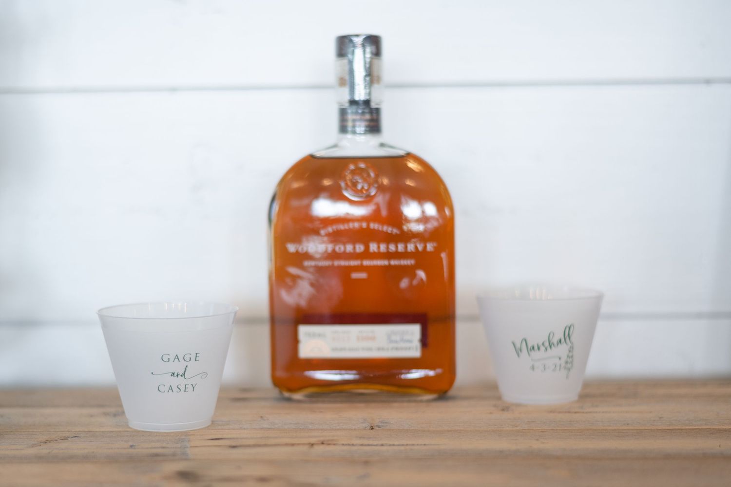 Bottle of bourbon with two small drinking glasses on a wooden surface.