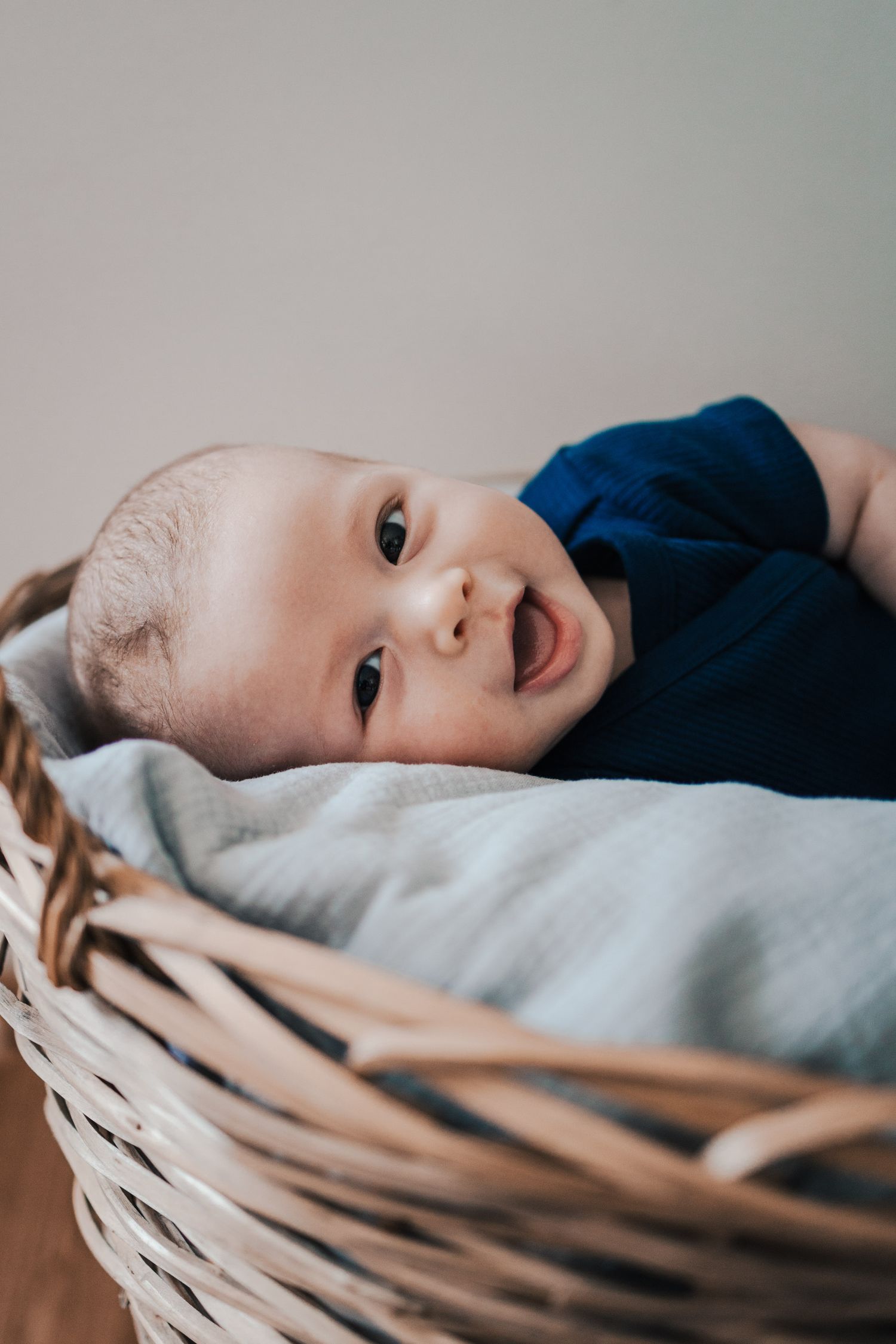 Sweet infant lying in woven basket wearing navy blue outfit.