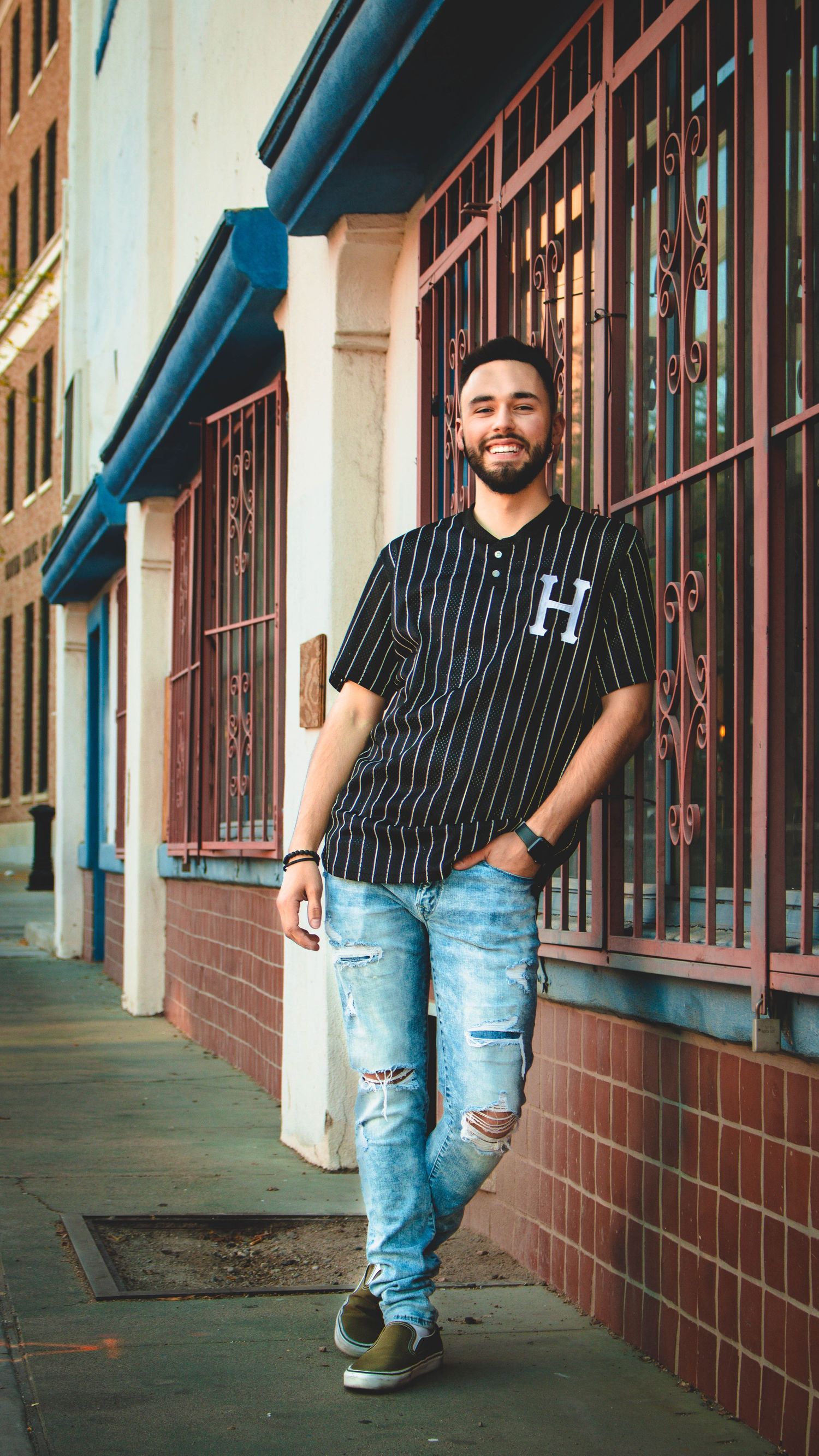 Urban fashion shoot featuring distressed jeans and pinstripe shirt against vintage building exterior.