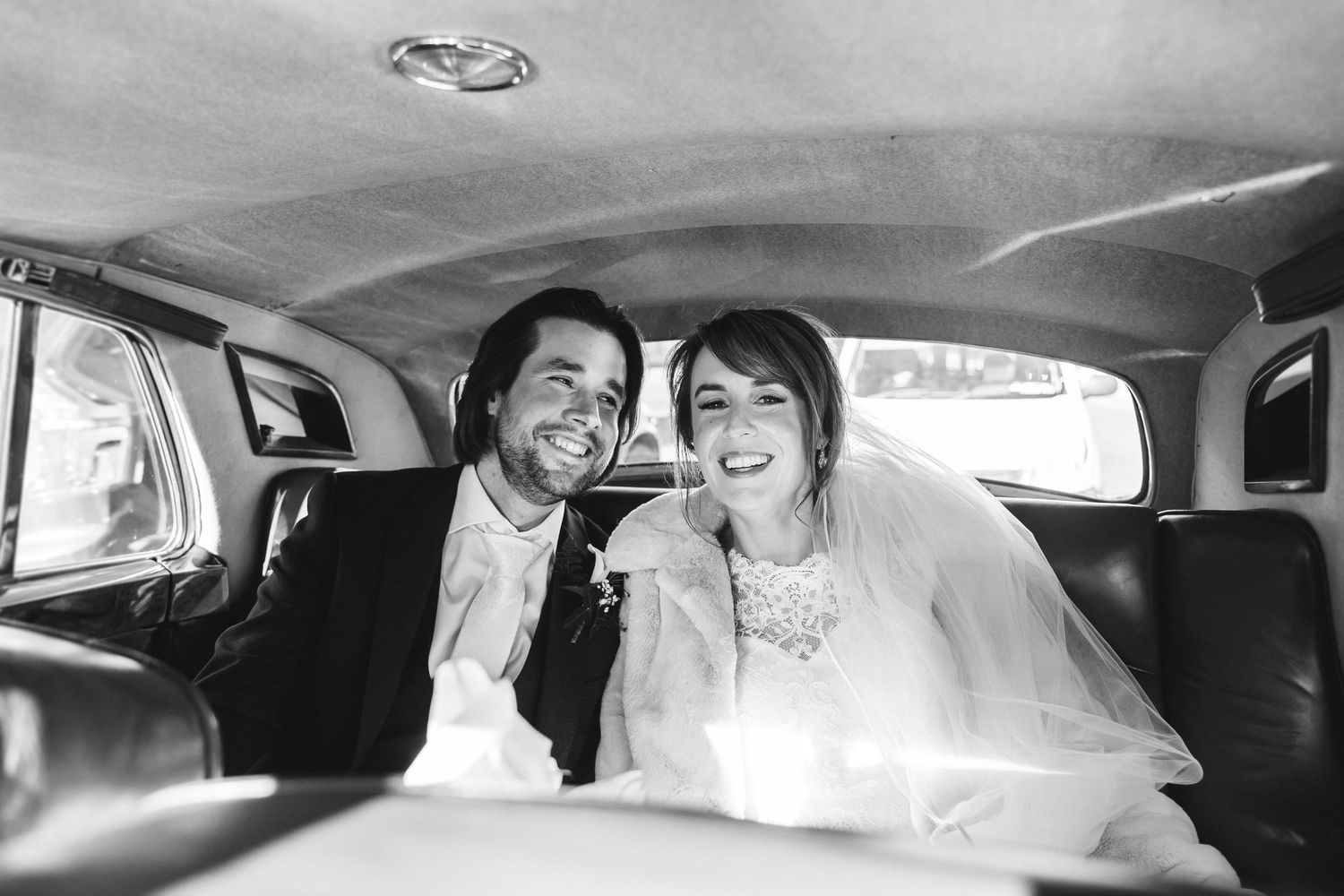 Vintage-style black and white photo of newlyweds sharing joyful moment in car.