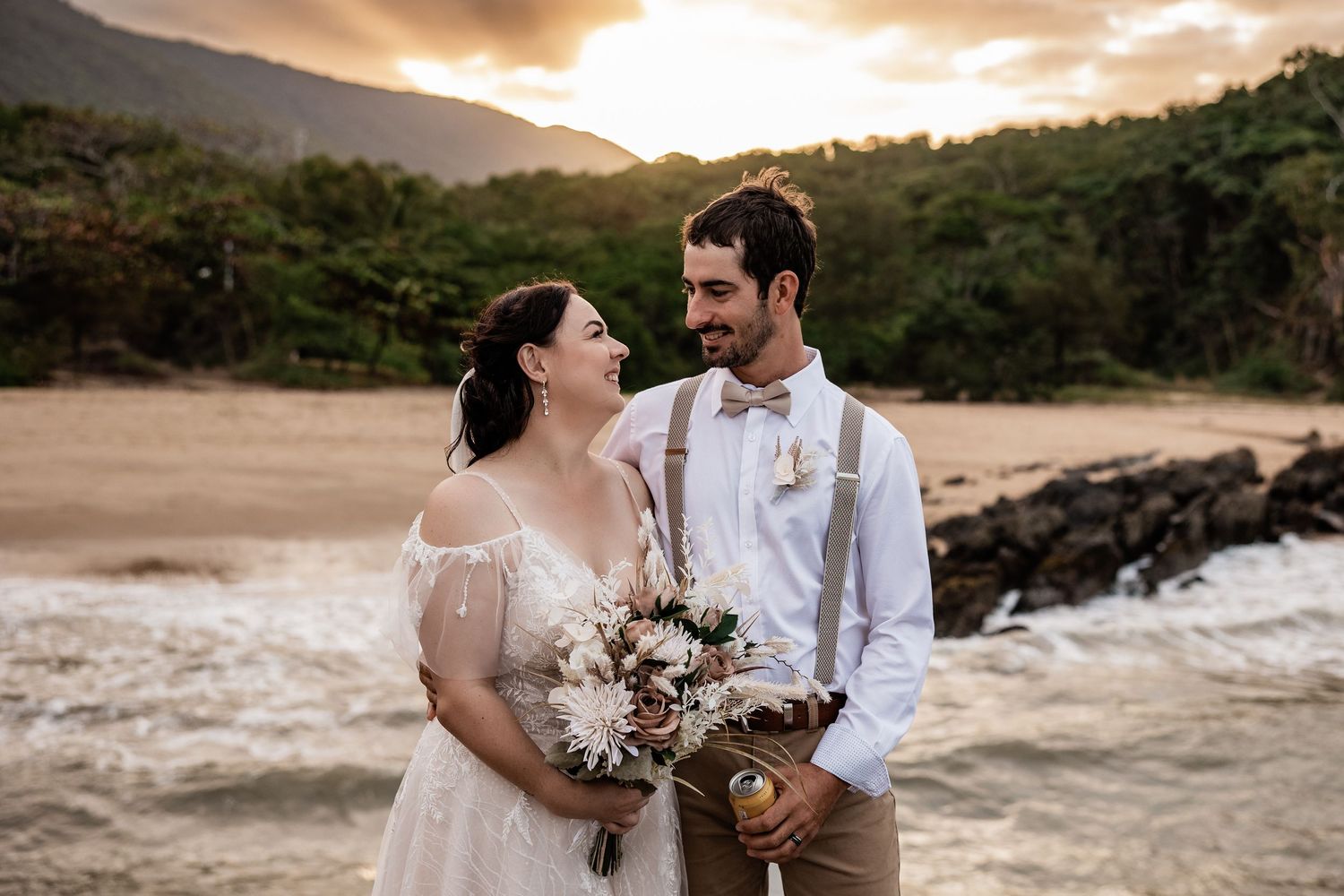 Couple in wedding attire sharing romantic moment on beach at sunset.