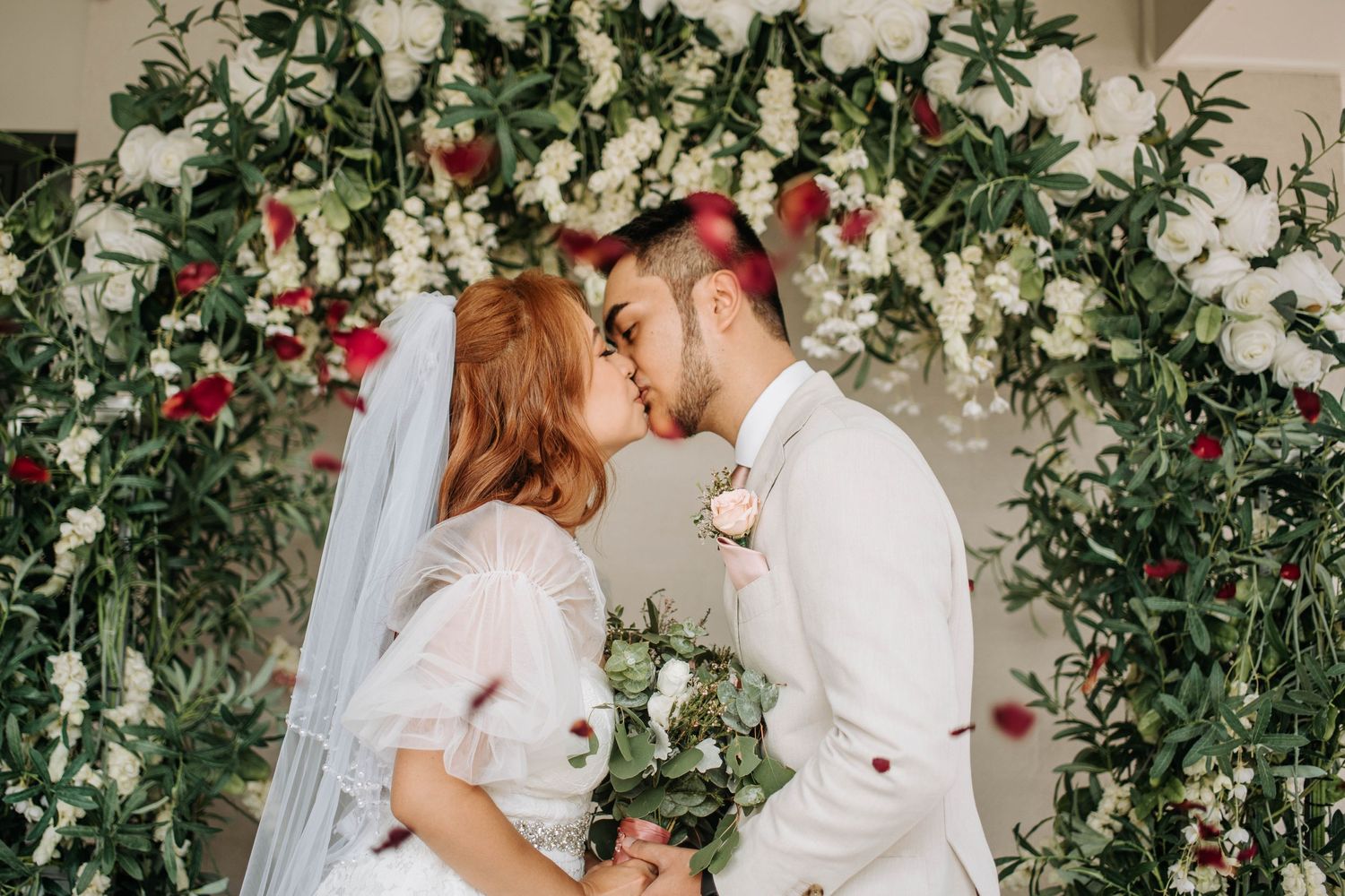 A romantic wedding ceremony moment under an arch decorated with white and pink flowers.