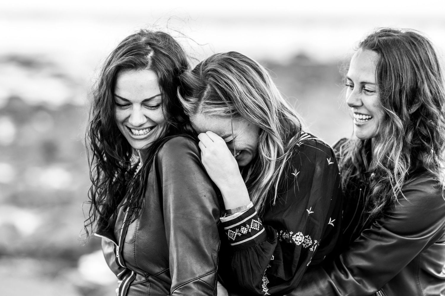 Black and white photo of three women laughing and embracing outdoors together.