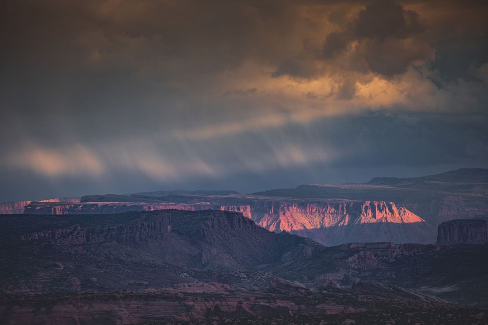 Stormy sunset illuminates red rock formations in the desert with dramatic clouds and shadows.