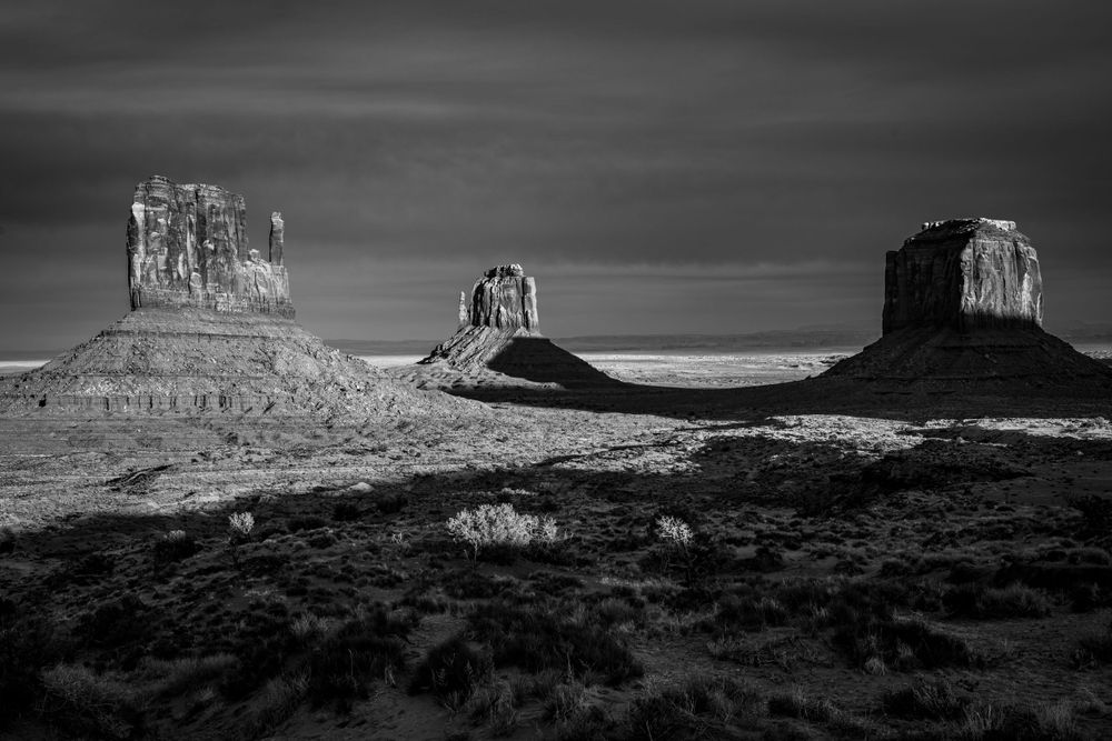 Dramatic black and white landscape of Monument Valley's iconic sandstone buttes against a moody desert sky.