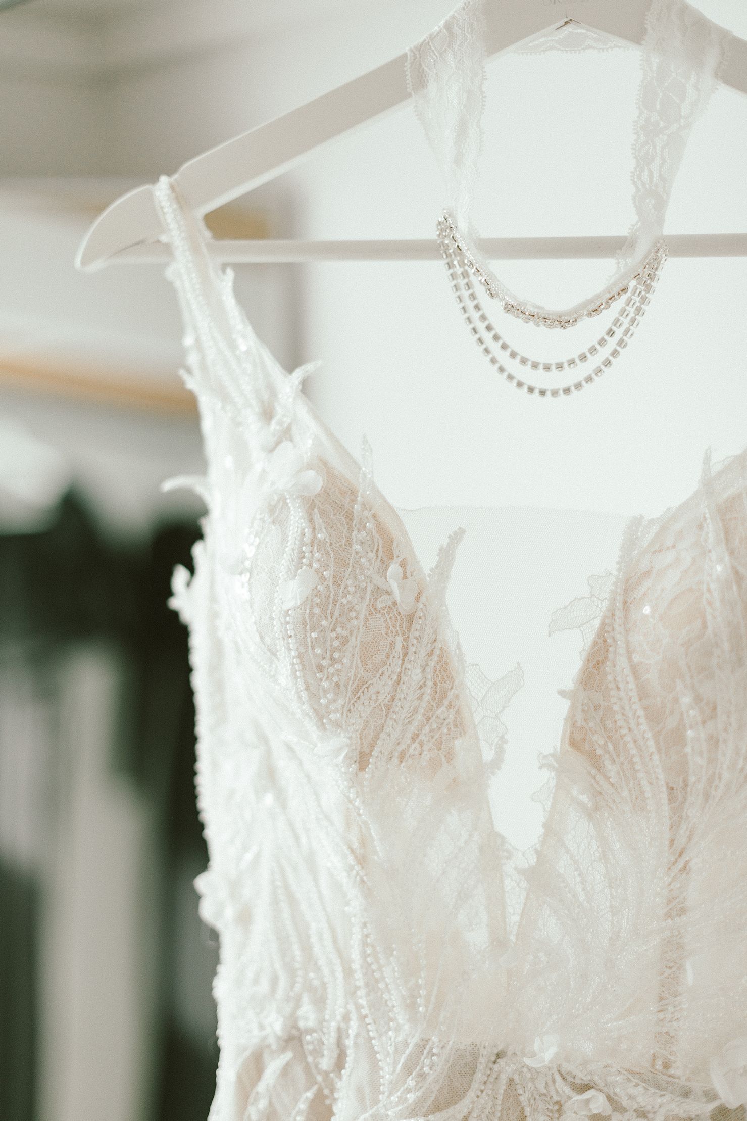 Close-up of white lace wedding dress bodice with pearl necklace hanging on display.