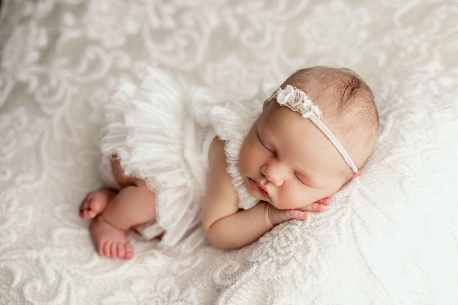 Sleeping newborn with lace headband lying on white textured blanket.