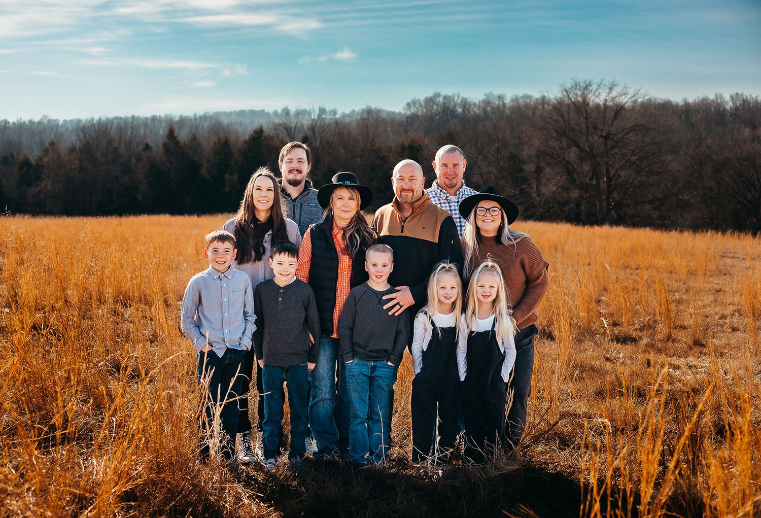 Extended family portrait of multiple generations posing together in autumn field.