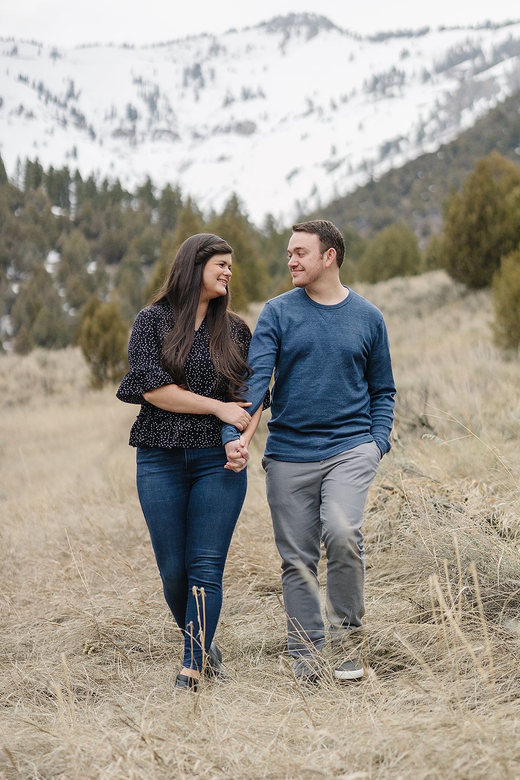 Couple walking together on mountain trail with snowy peaks in background.