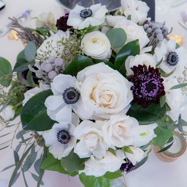 Elegant wedding centerpiece with white roses, anemones, and eucalyptus in soft purple and white tones.