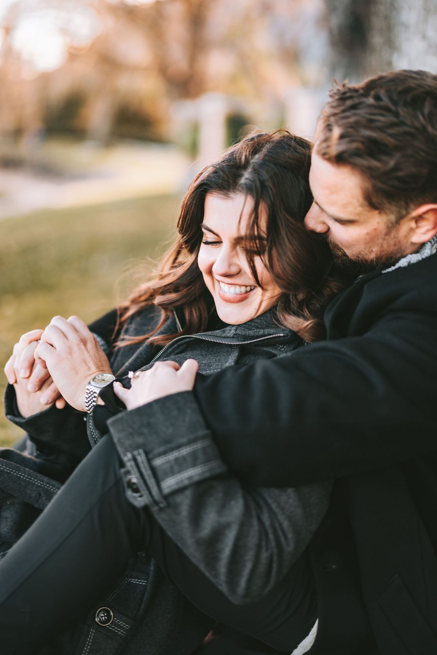 Intimate autumn moment captured of a couple in black coats sharing a joyful embrace.