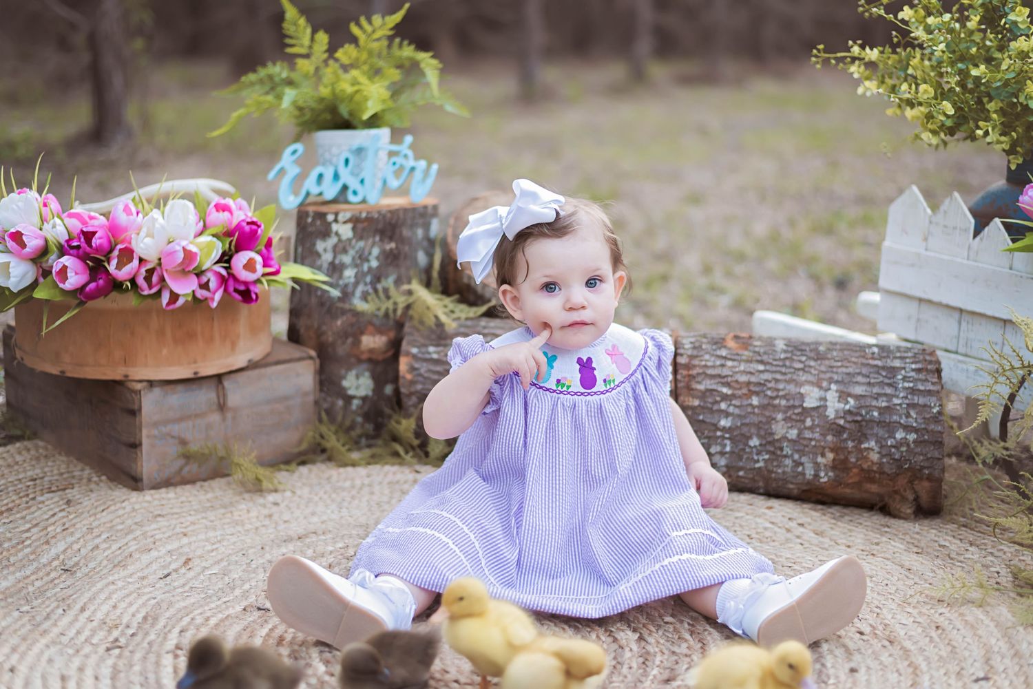 Child in purple dress sits among spring flowers during outdoor photo session.