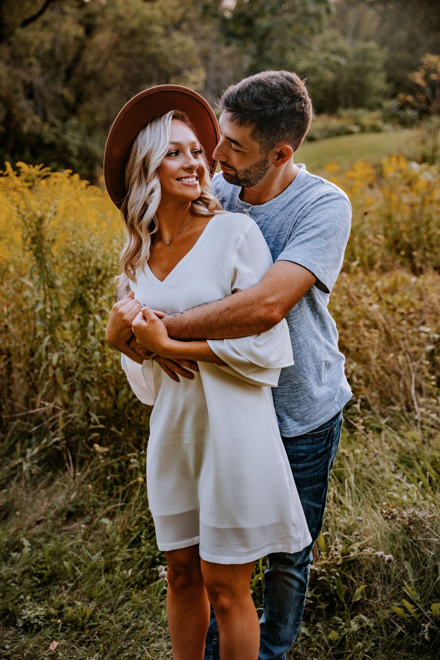 A couple embraces in a golden field during sunset with autumn colors surrounding them.