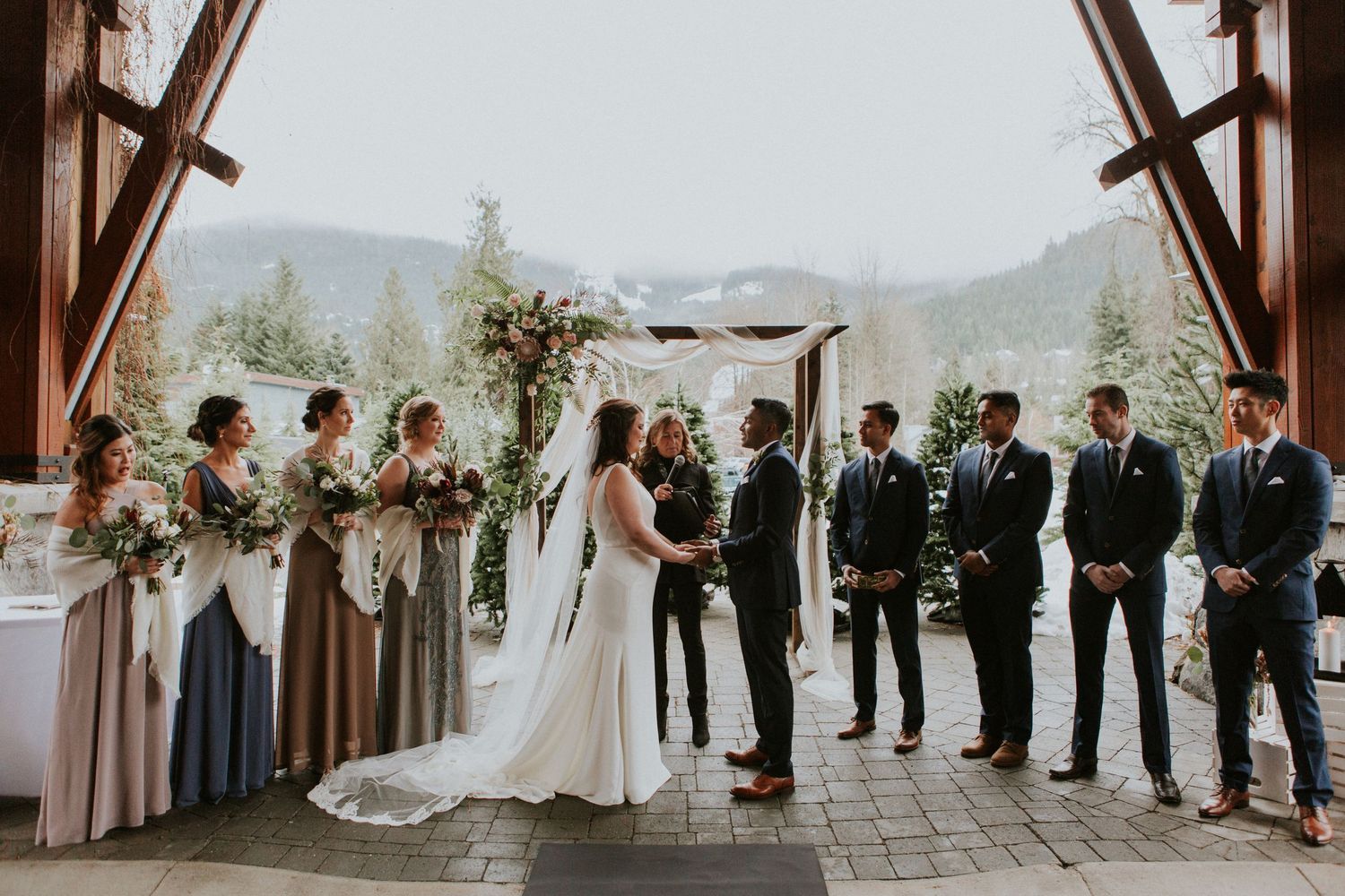 A wedding ceremony taking place under a wooden arch with mountain views and floral decorations.