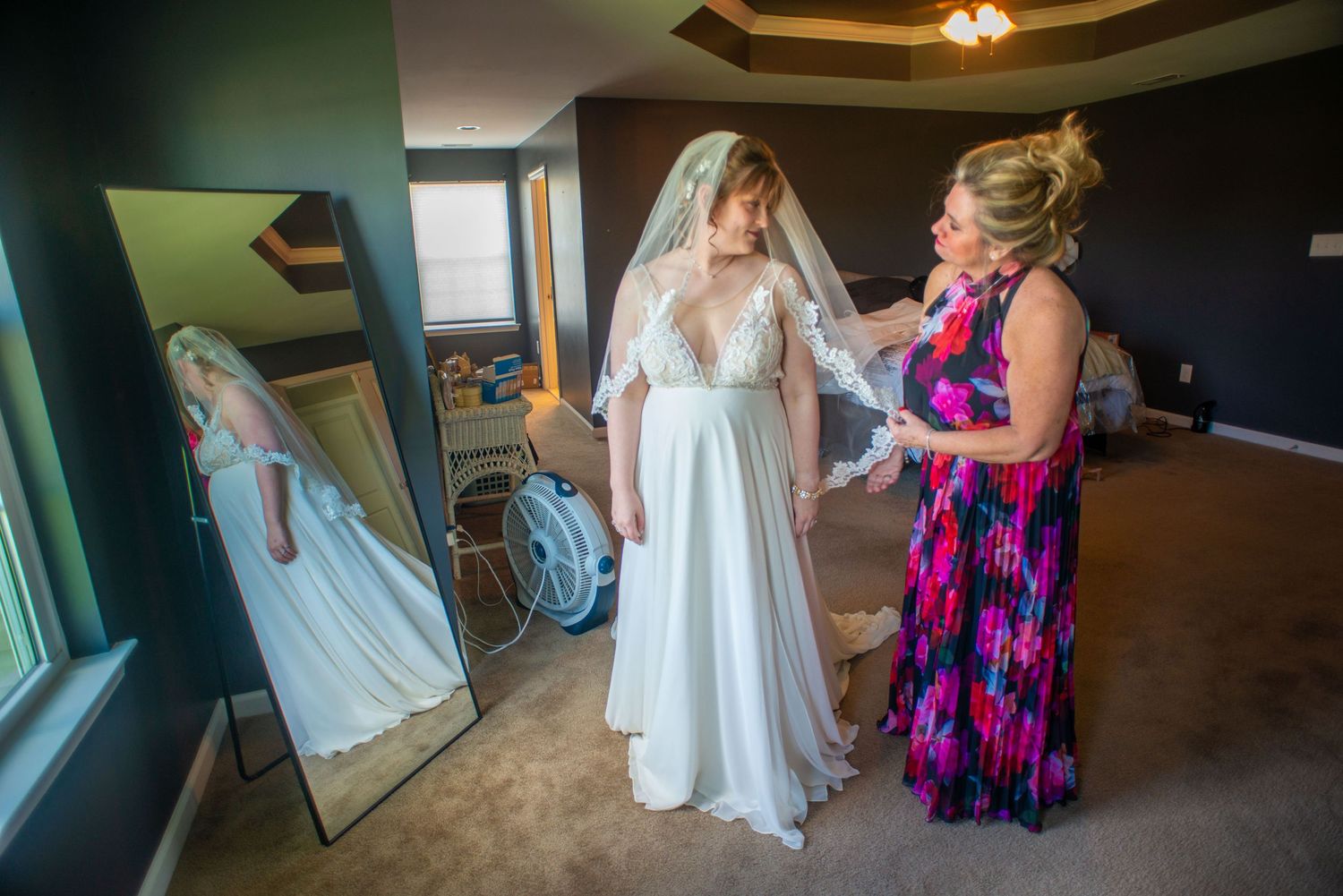 Wedding dress fitting and final adjustments in bridal suite with mirror reflection.