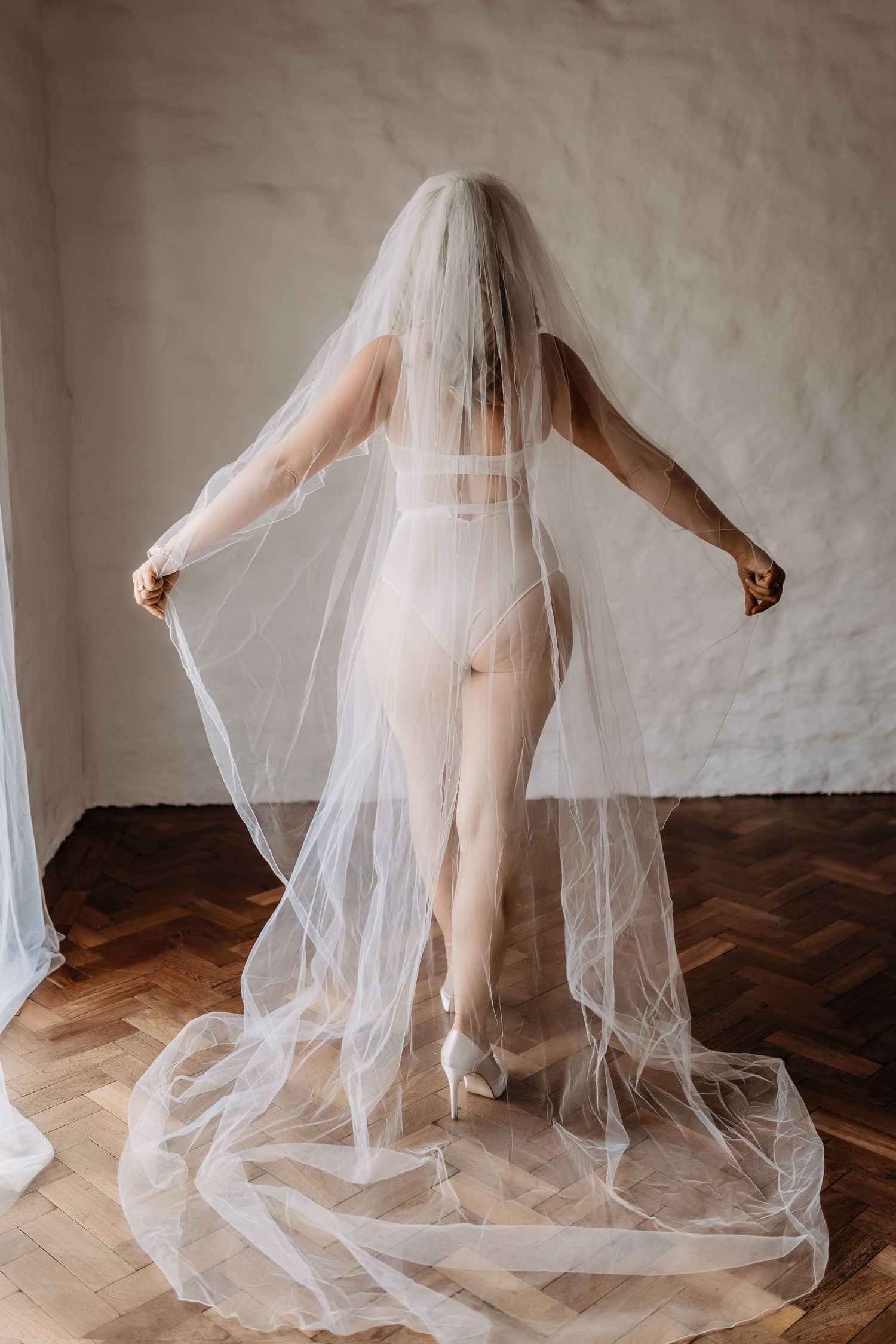 Artistic silhouette of bridal attire with flowing cathedral veil against wooden floor.