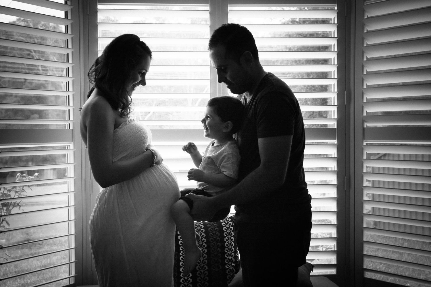 Toddler touching mums pregnant belly held by dad