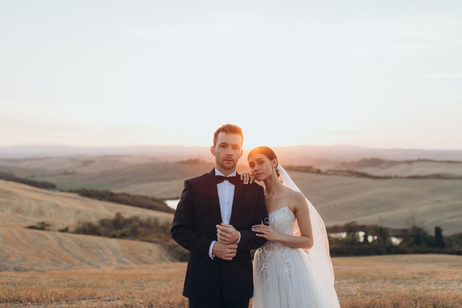 Wedding couple in formal attire posing together at golden hour on a scenic hillside.