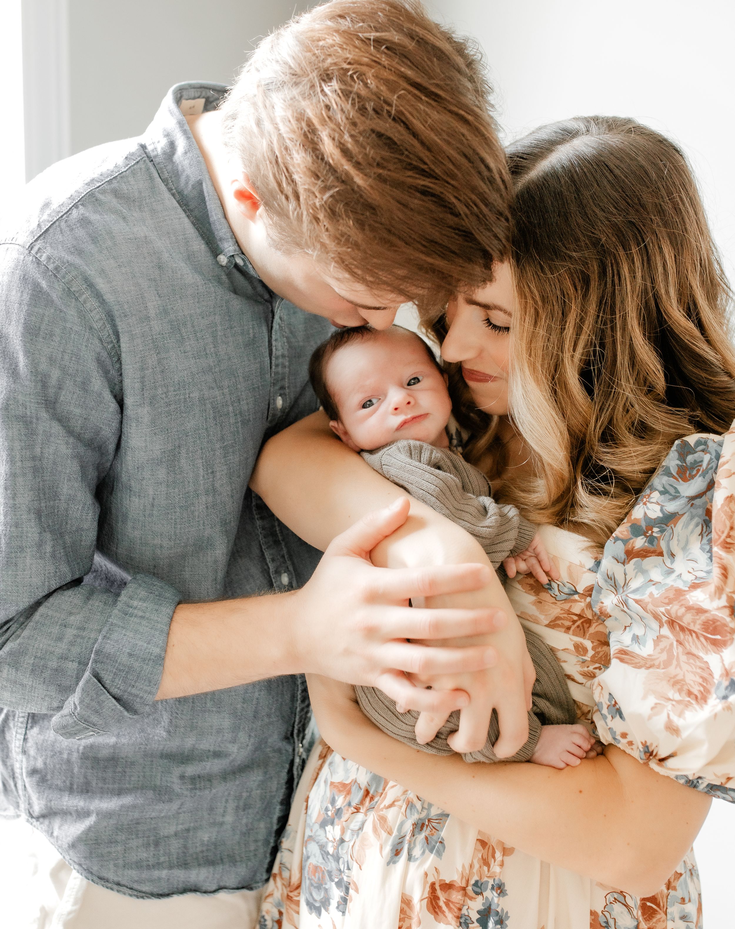 A tender family moment as parents cuddle with their newborn baby in an intimate indoor portrait.