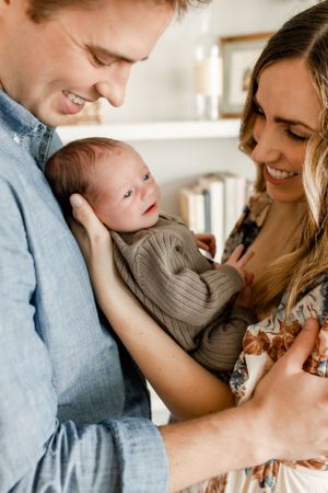 Parents gazing lovingly at newborn baby in casual home setting.
