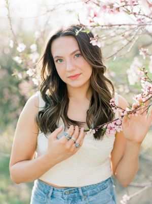 Brunette teenage girl looking at camera surrounded by pink cherry blooms