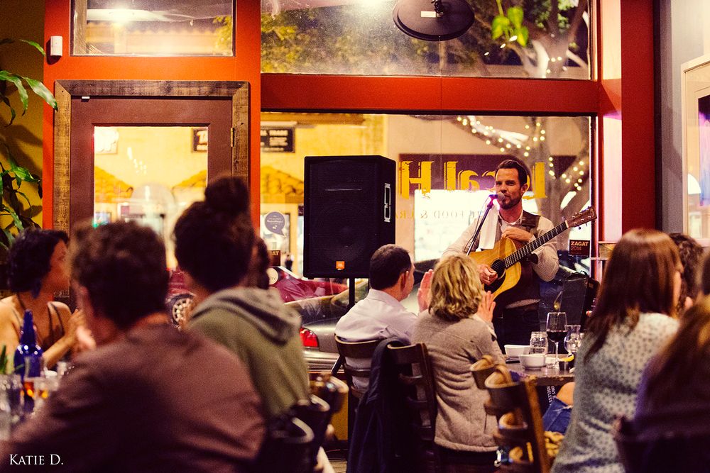 A live acoustic guitarist performs for a crowd of diners at a casual restaurant.