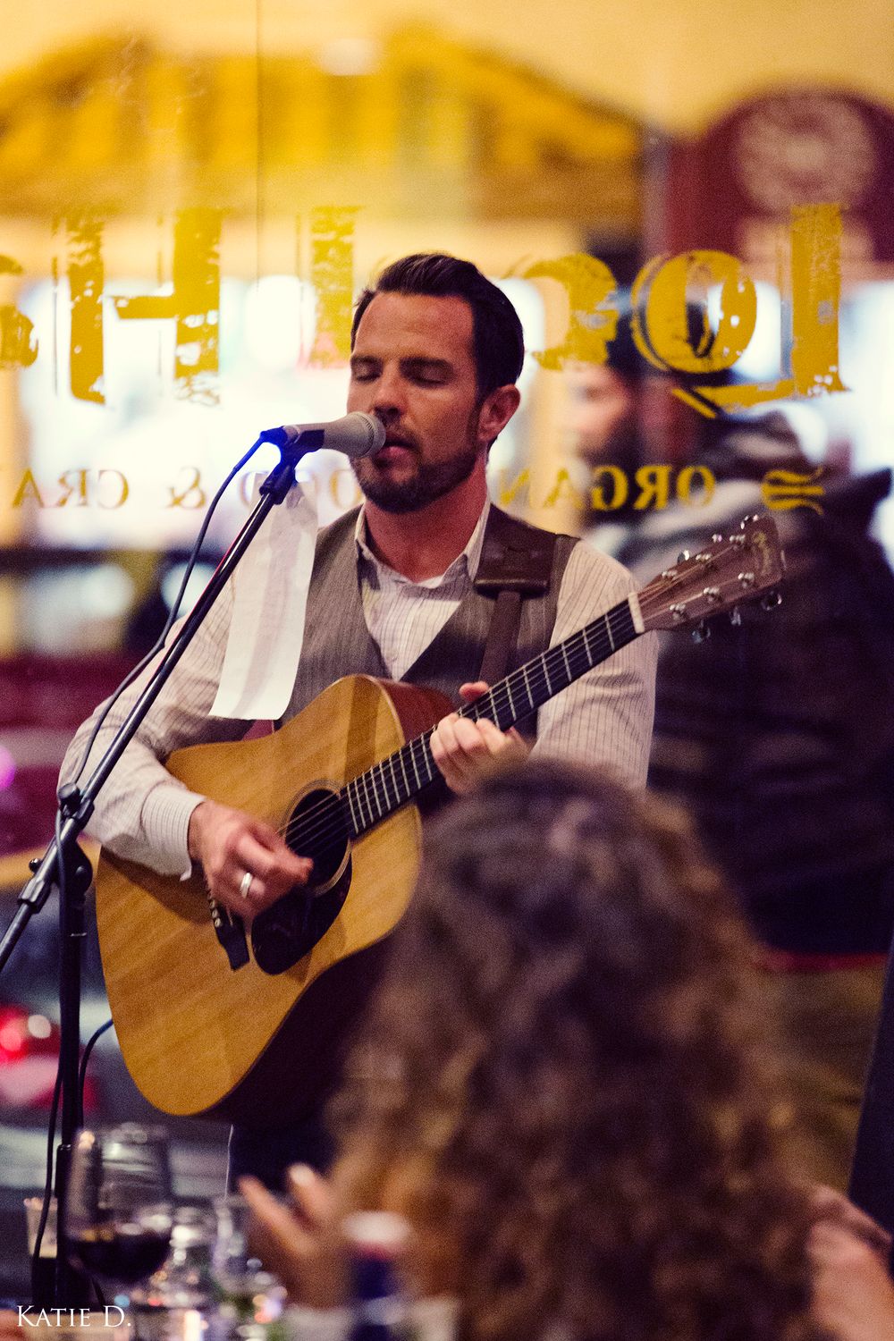 A focused male guitarist sings into a microphone during a live performance at a restaurant.