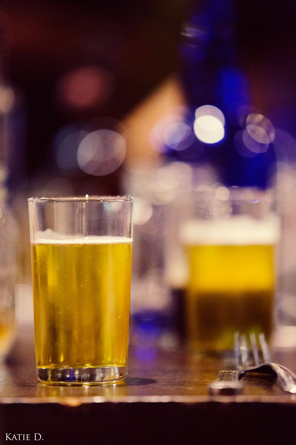 Two glasses of golden craft beer sit on a wooden bar table with bokeh background.