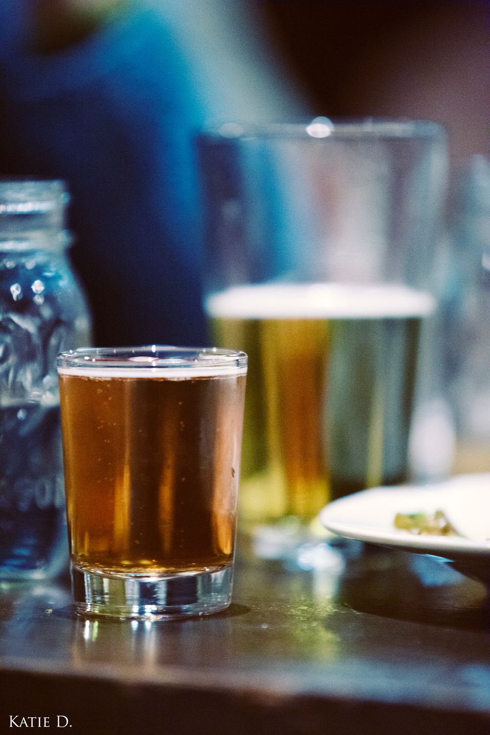 Close-up of a glass of craft beer on a restaurant table with blurred glasses in background.