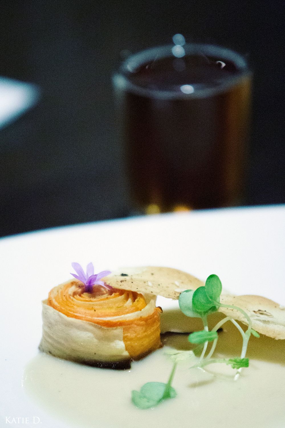 Elegant plated dish with spiral pastry, edible flower, and microgreens on white plate.