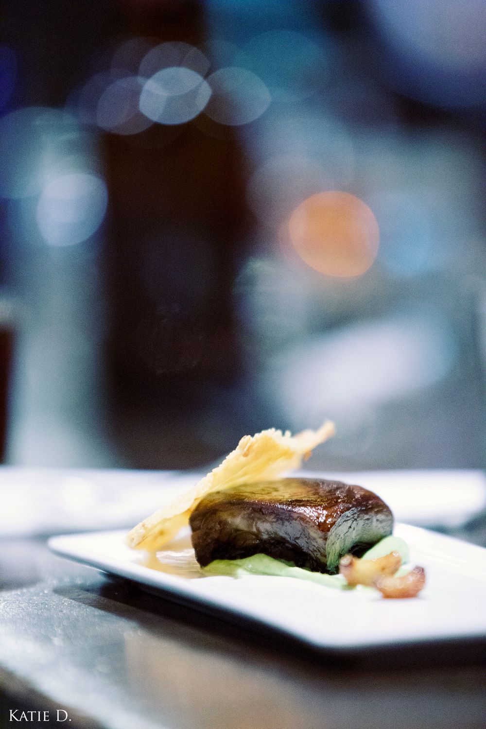 Gourmet meat dish served on white rectangular plate with garnish and bokeh background.