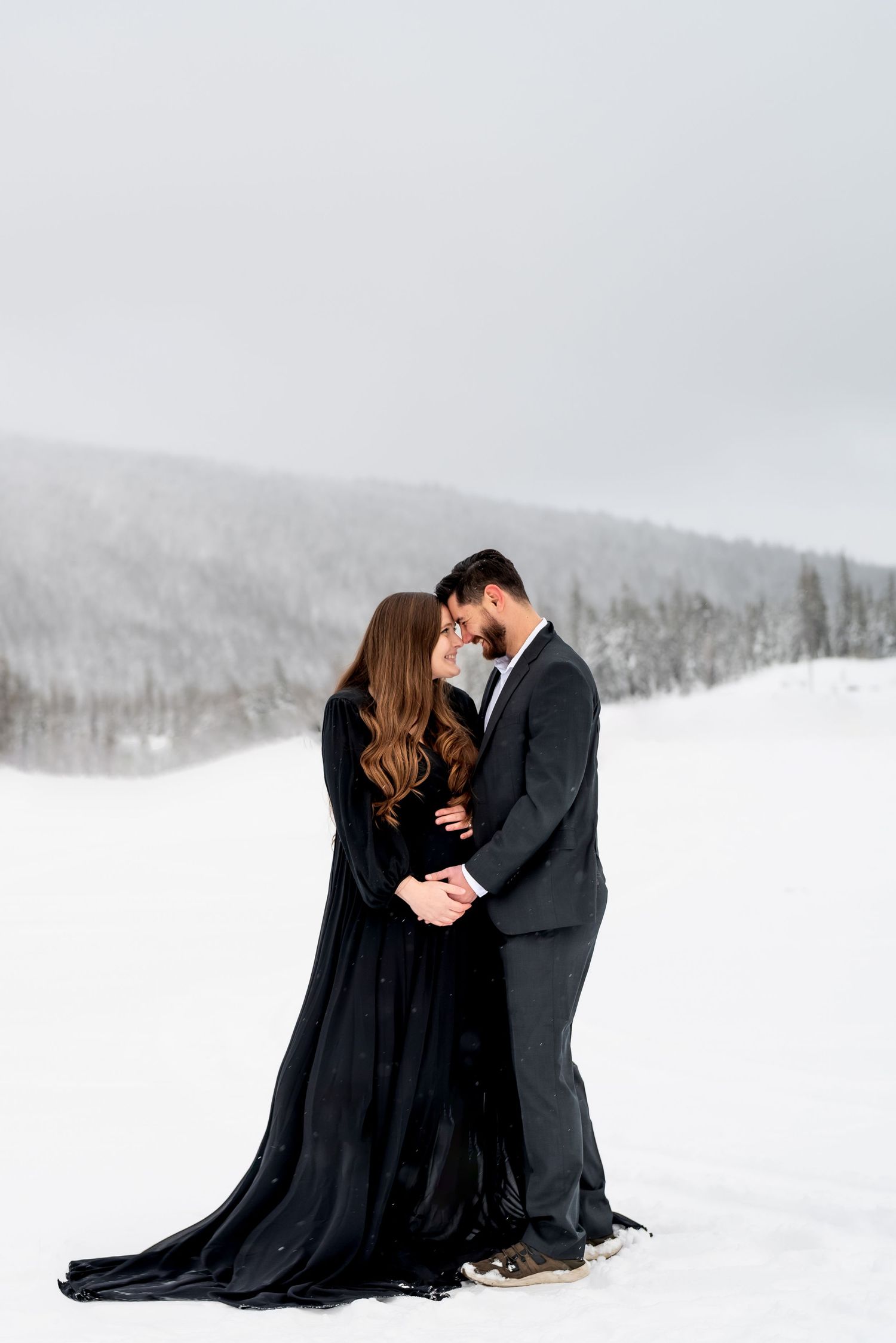 Romantic couple in black attire embracing in a snowy winter landscape.