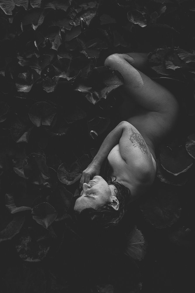 Artistic nude photography with dramatic lighting and leaf shadows creating mood.