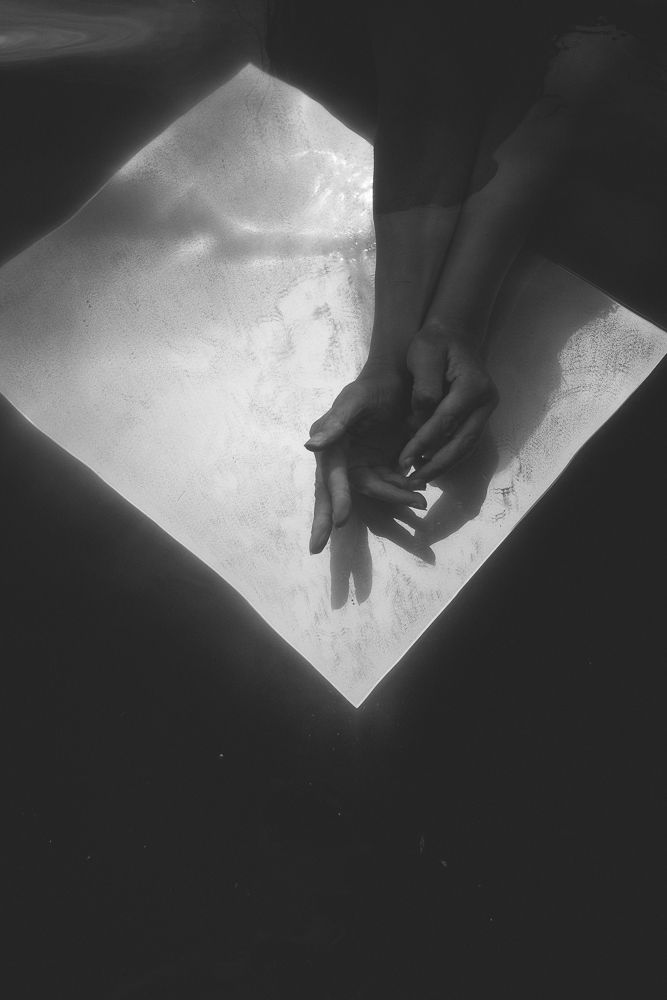 Artistic black and white photo of hands touching against a bright geometric background.