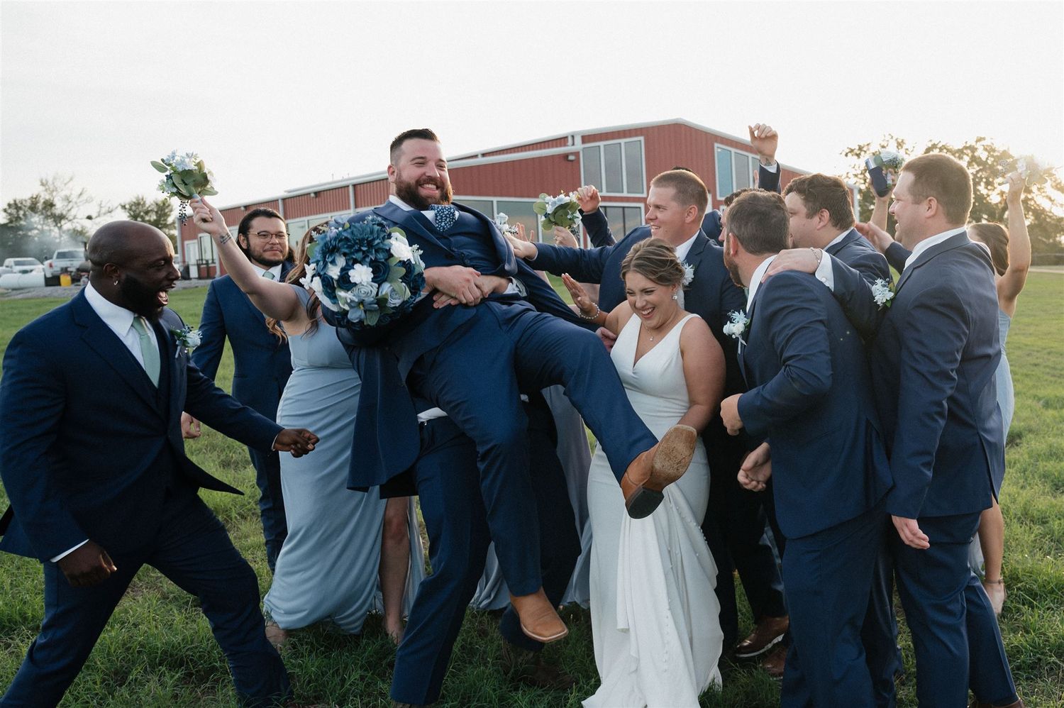 Groomsmen playfully lifting groom during outdoor wedding photo session.