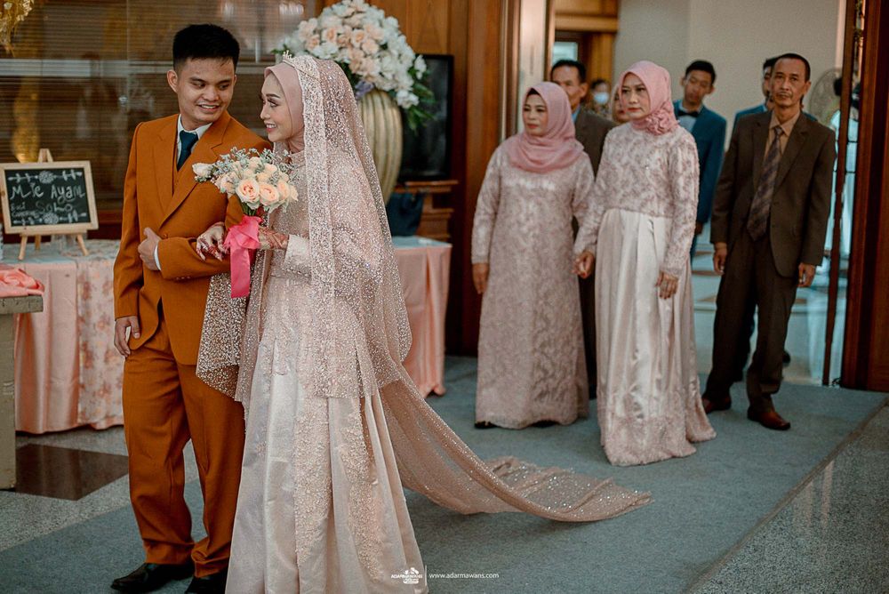 Wedding couple and guests in formal attire with the groom in orange suit and bride in flowing pink lace dress.