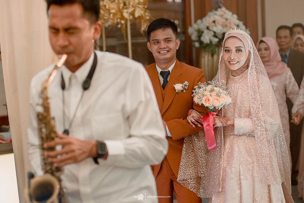 A saxophonist performs at a wedding reception while the couple stands in the background.
