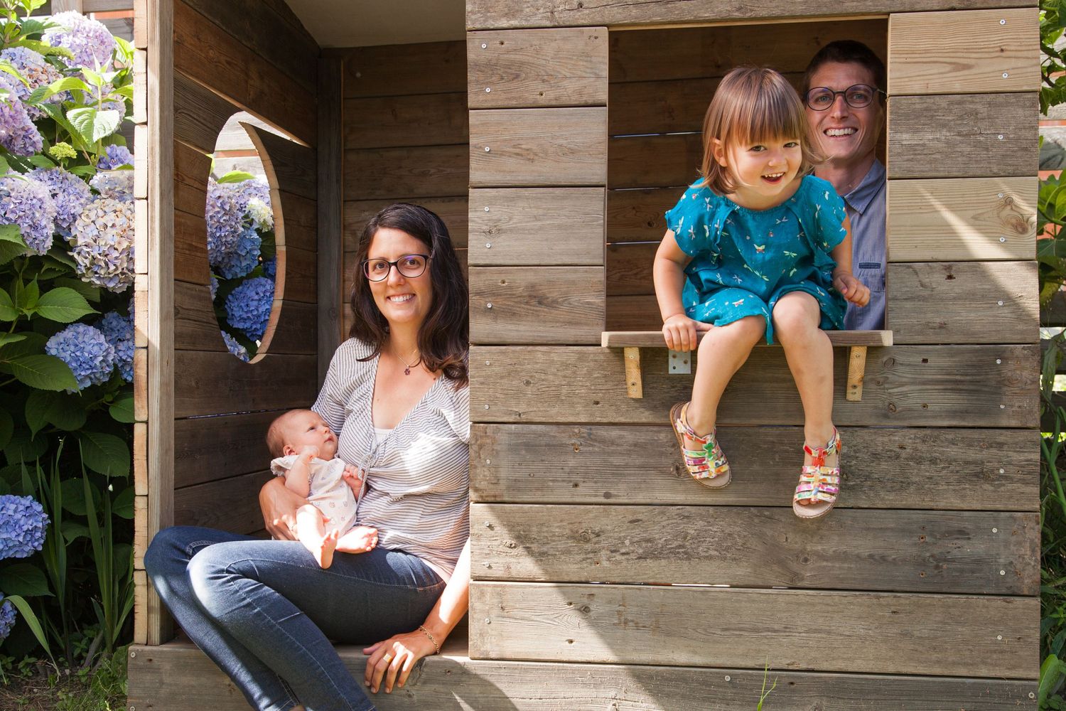 Une famille avec une petite fille et un bébé posent dans la cabane au fond du jardin.