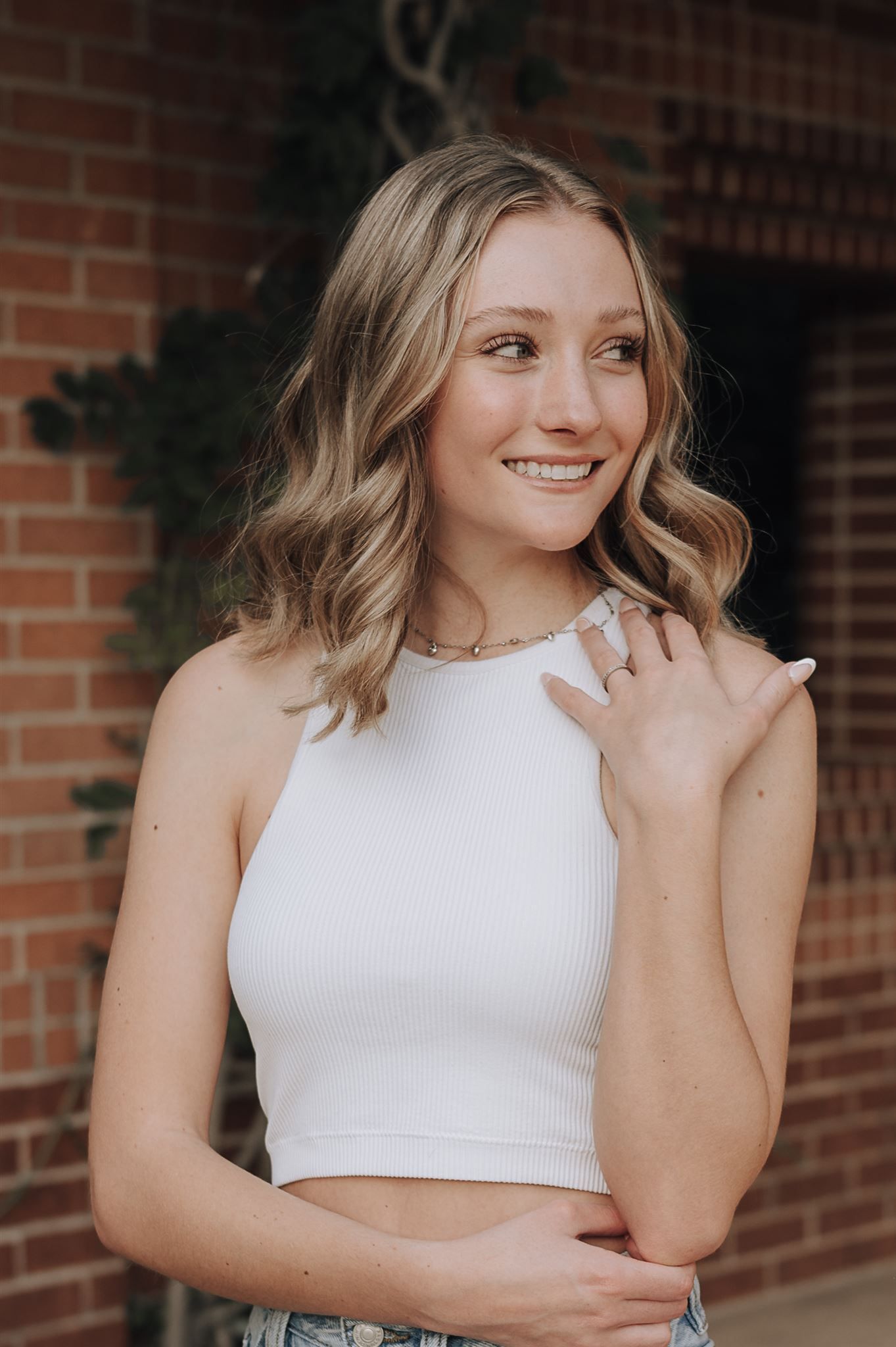 Casual portrait in white halter top with wavy hair against red brick wall.
