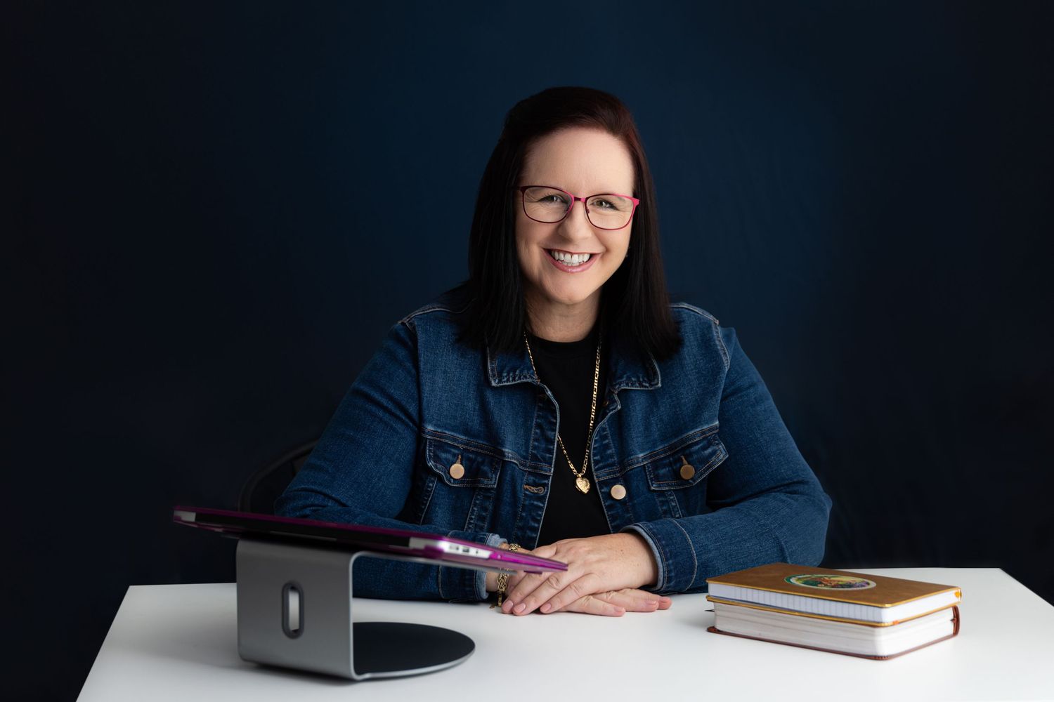 Professional studio portrait with laptop and books on white desk.
