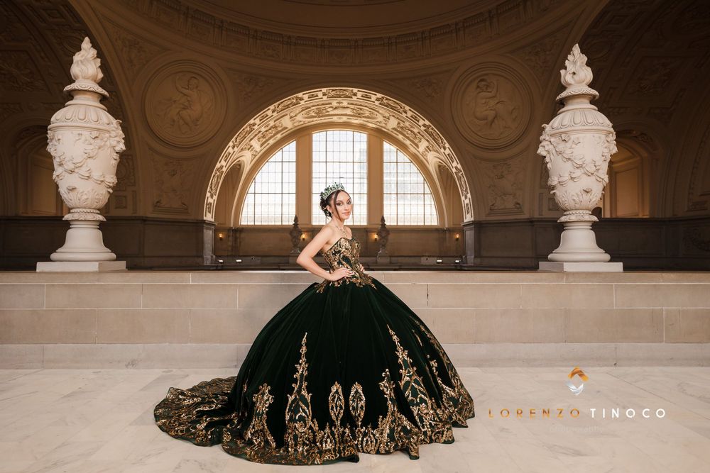 Ornate black ballgown with gold details photographed between classical white sculptures in grand hallway.