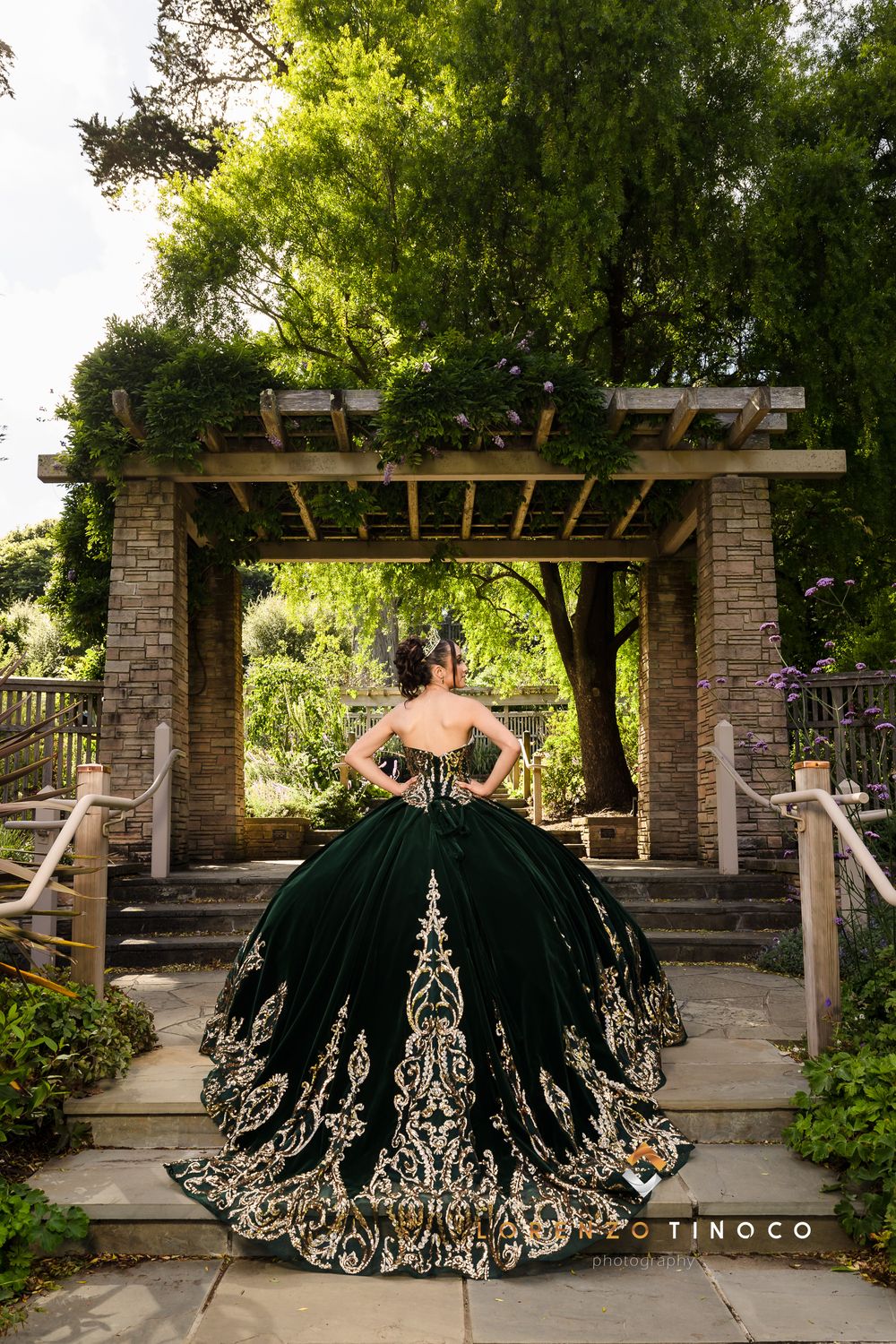 Dramatic black and gold quinceañera dress showcased under garden pergola with stone pillars.