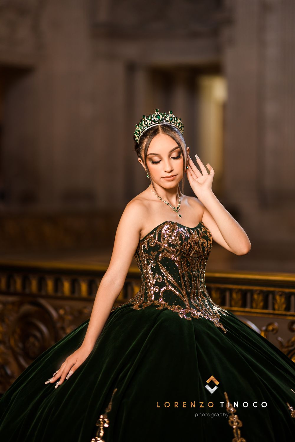 Stunning dark green ball gown with intricate gold embroidery and crystal tiara in an elegant indoor setting.