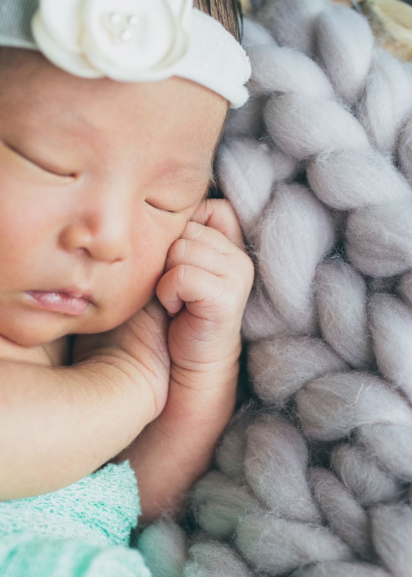 Peaceful sleeping newborn with white headband lying on soft gray knit blanket.